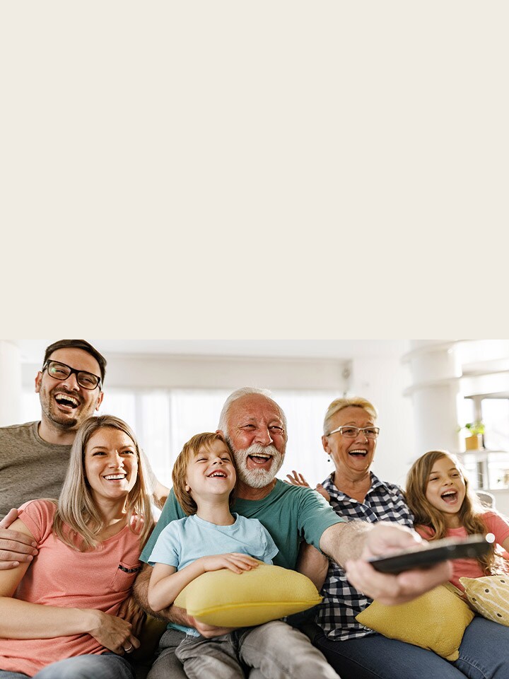 Une famille est assise et rit, tandis que le grand-père dirige la télécommande vers l’extérieur.