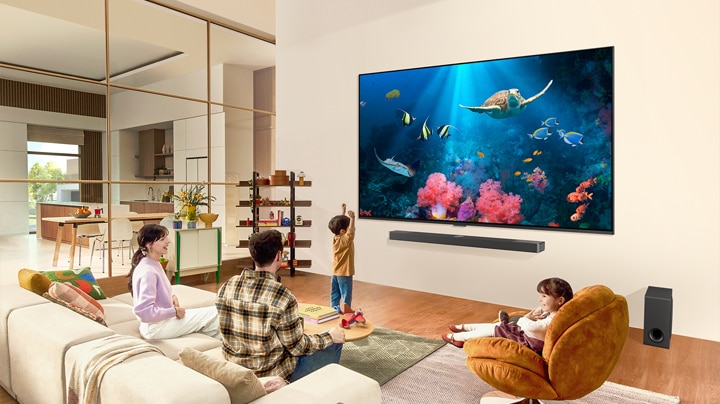 Une famille dans un salon avec un très grand téléviseur LG fixé au mur, avec une scène d'océan comprenant du corail et une tortue sur l'écran.