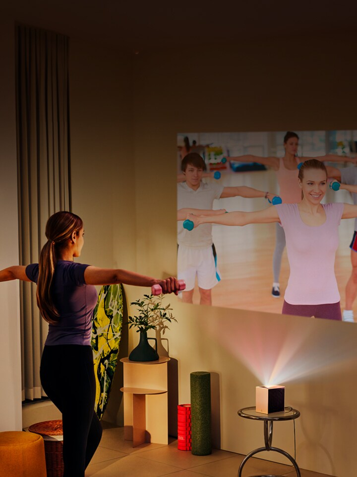 Une femme faisant du yoga avec une projection du LG CineBeam en arrière-plan.