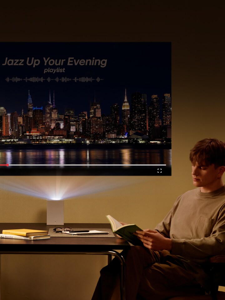 Homme lisant un livre avec une projection du LG CineBeam en arrière-plan.	