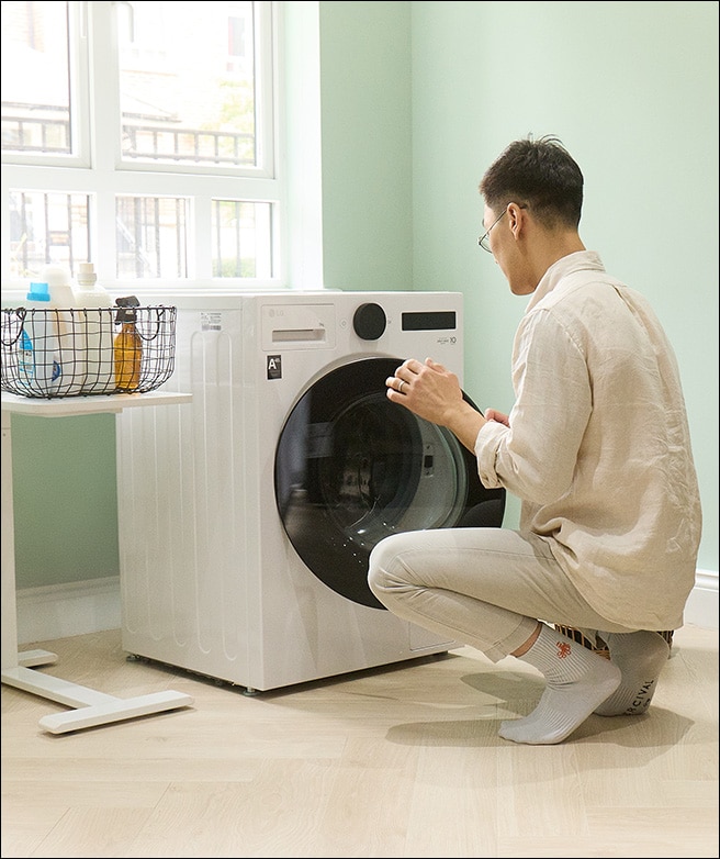 Homme chargeant le linge dans une machine à laver tout en réglant les paramètres.