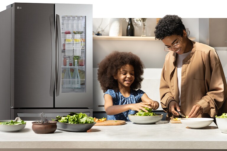 Un adulte et un enfant préparent à manger dans la cuisine, avec un réfrigérateur éclairé