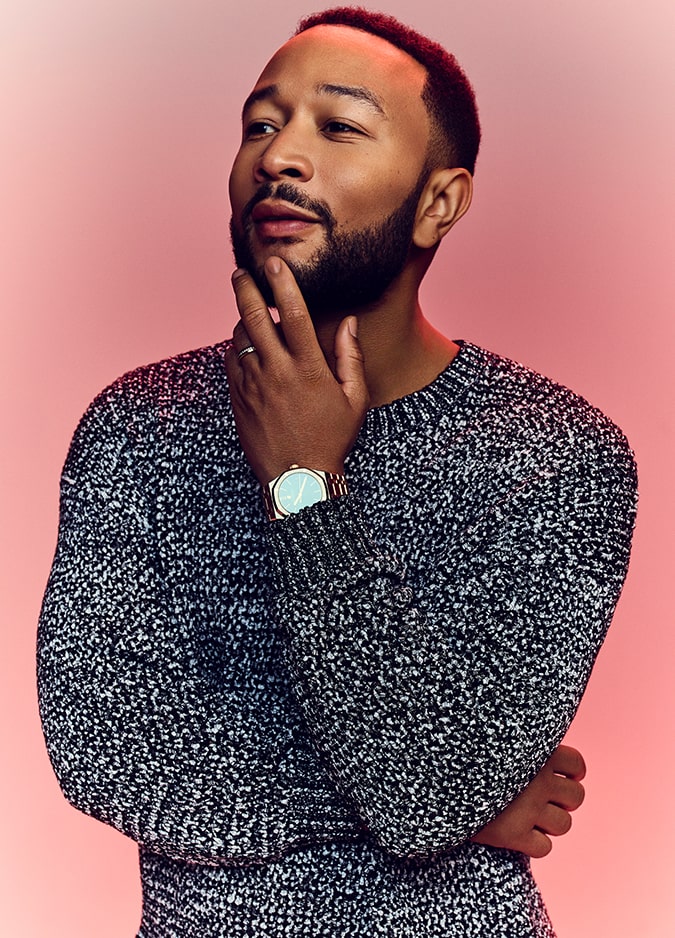 Picture of John Legend touching his chin against a red background.