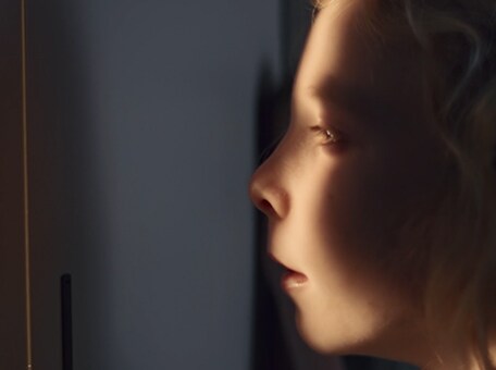 A close-up shot of a girls face, partially in shadow, partially illuminated as she peers out from a hiding place.