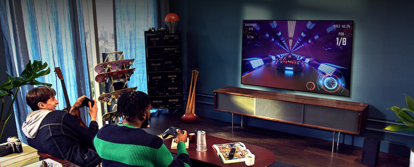 Two people sit on a couch playing a racing game with a controller and LG SIGNATURE OLED 8K in a living room.