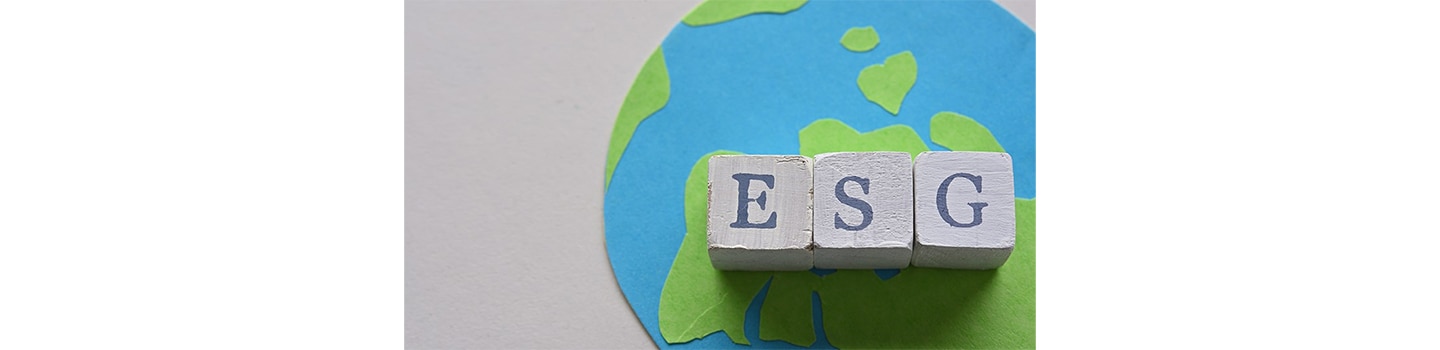Three cubes displaying letters from the acronym ESG stand on top of a handmade picture of the world.