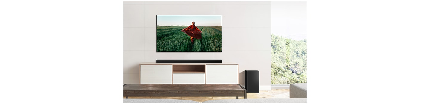 LG Soundbar sitting on a wooden cabinet below the wall-mounted LG TV to complement the TV's sound while blending effortlessly into the earthy room décor