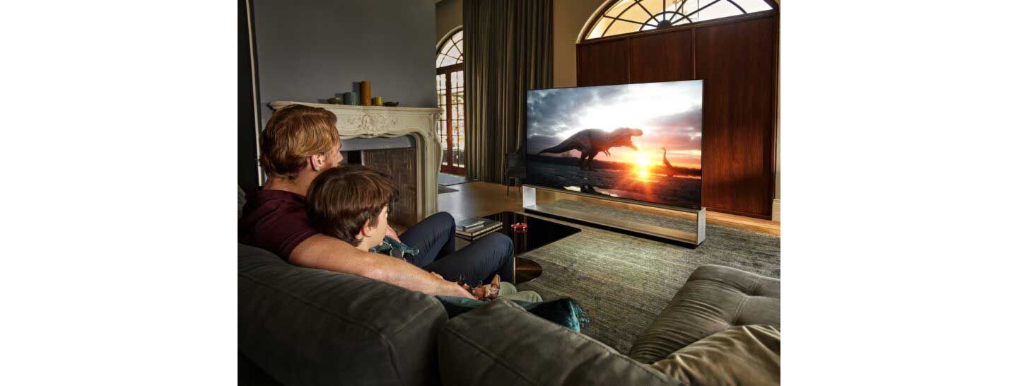 Father and son sit together in their living room to watch dinosaurs come to life on their LG TV.