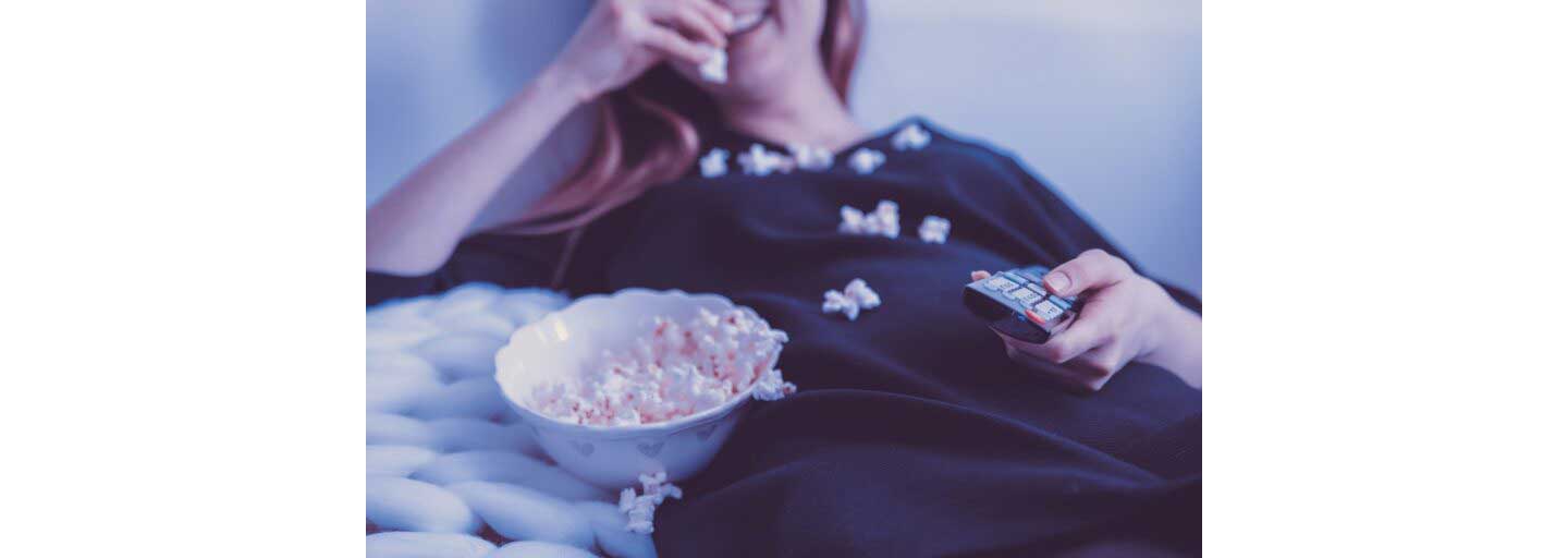 A woman holding the TV remote while eating popcorn.