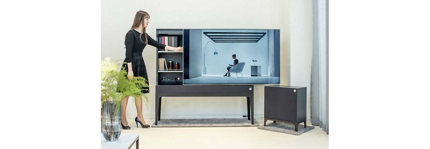 A woman slides open the display panel of LG Objet TV in order to use the storage hidden behind the panel