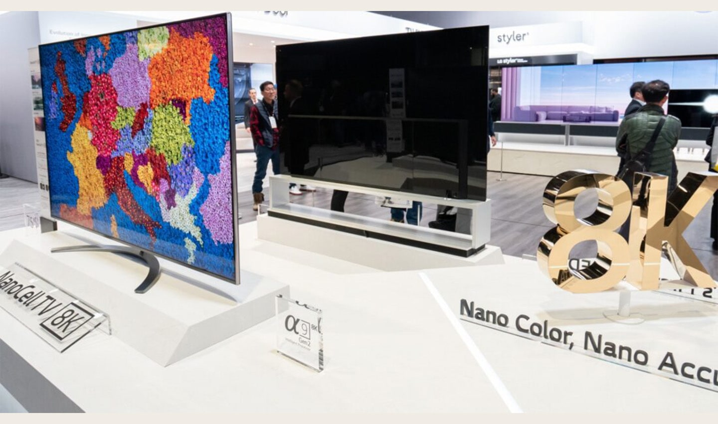 Two LG 8K NanoCell LCD TV models that are positioned the front and the back next to a rotating 8K promotional sign board