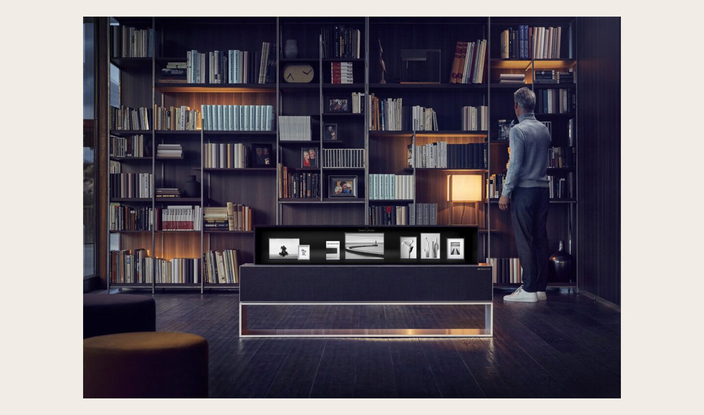 A man is browsing his bookshelf, an LG SIGNATURE OLED TV R enhances the environment by displaying photos on its screen