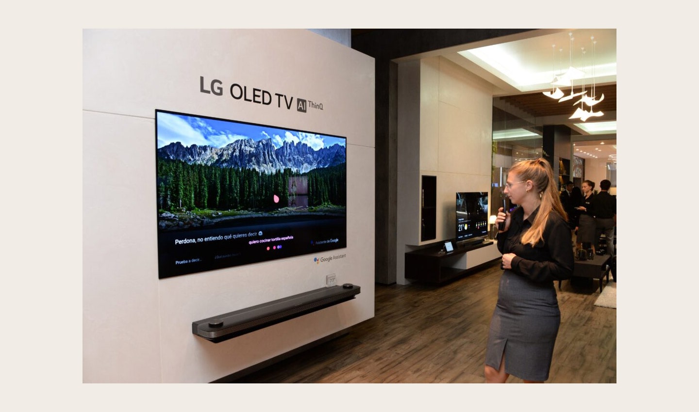 View of LG OLED TV AI ThinQ display zone, a female attendant tries out the TV's AI voice assistant features with the Magic Remote