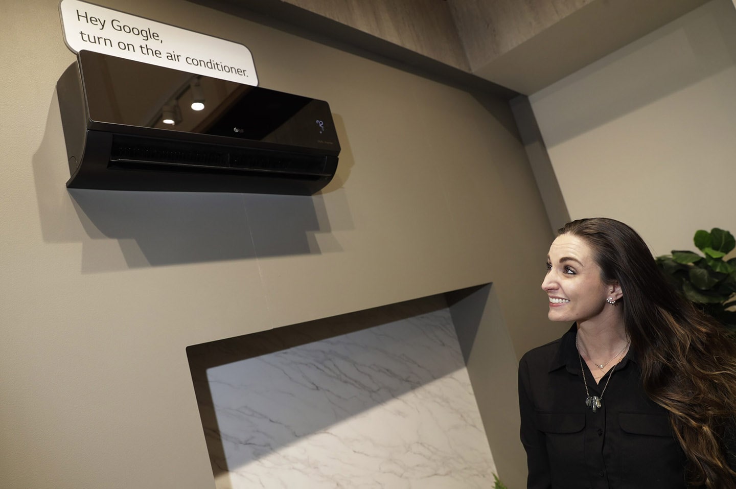 Woman looking up at a black LG air conditioner with a sign that says “Hey Google, turn on the air conditioner”