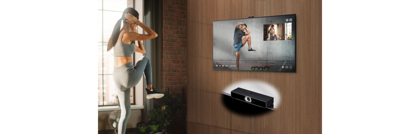 A woman using a fitness application on her LG TV to exercise at home, with LG Smart Cam attached to the top of the TV