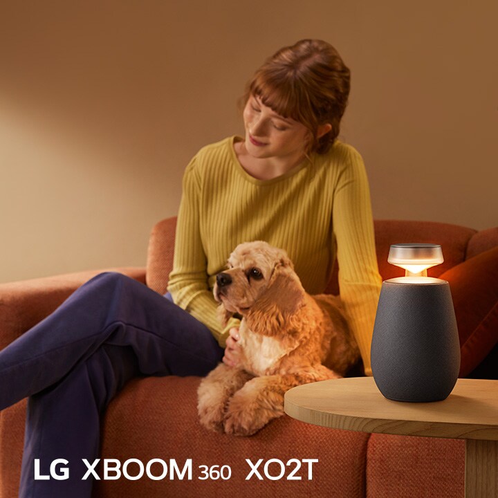 一位女士和她的狗坐在沙發上,用 LG XBOOM 360 XO2T 聽音樂。