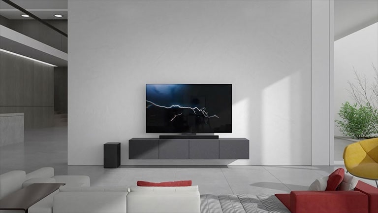 Sound Bar 與電視擺放在客廳的灰色櫃上。黑色無線重低音喇叭擺放在左邊地板上，陽光從圖片的右邊照射進來。紅白色長沙發擺放在面向電視和 Sound Bar 的位置。