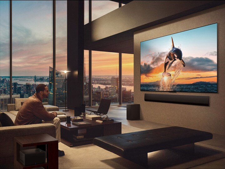 窗外為城市景觀的寬敞客廳。掛牆安裝的 LG OLED 電視及 LG Soundbar。電視的 One Wall Design 使其可無縫貼合牆身,與空間完美融合。Zero Connect Box 巧妙隱藏其中。