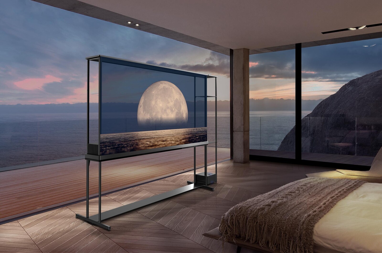 LG SIGNATURE OLED T 在透明螢幕上顯示描繪在海岸上方的月亮。LG SIGNATURE OLED T 置於房間中央，可看到懸崖邊的海景。右邊是一張床和一張躺椅。