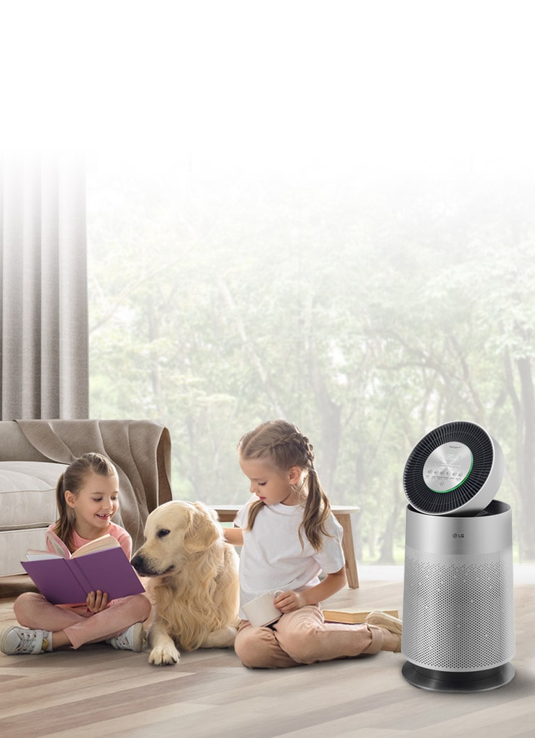 Two children sit on the floor, one reading beside a golden retriever and an LG air purifier, in a room with large windows.