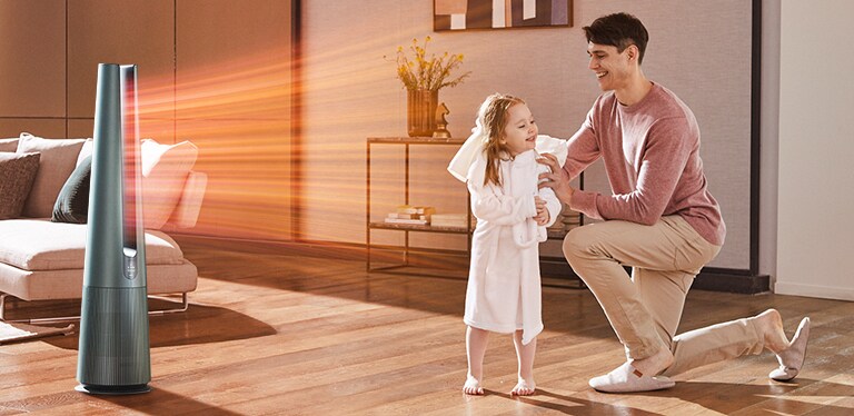 Man kneels in cozy living room helping child in bathrobe, with LG air purifier blowing warm air towards them.