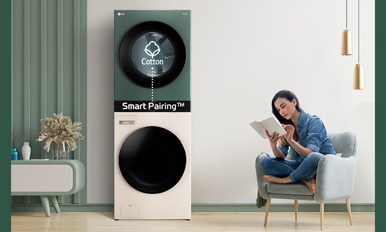 LG stacked washer and dryer with Smart Pairing feature in a modern room, next to a person sitting on a chair reading a book.