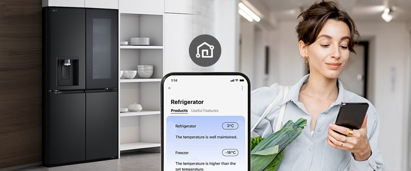 Woman holding groceries uses her phone to check the temperature of an LG smart refrigerator in her modern kitchen.