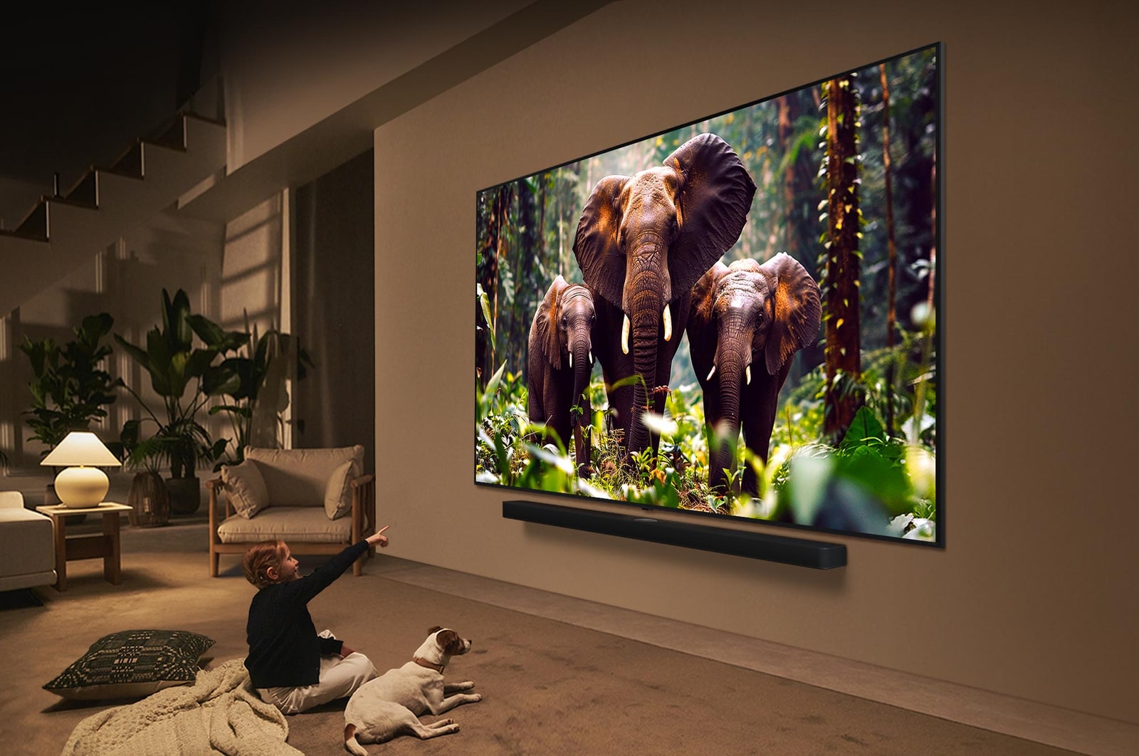 A girl and a dog are seated in front of a LG QNED TV mounted on a wall depicting three elephants walking outwards above a LG Soundbar. The title talks about how every action is more thrilling on a massive screen.