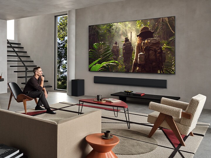Tampilan ruang tamu yang luas di dalam rumah mewah, sepasang suami istri sedang menonton film di LG OLED TV wall mounted. Desain TV berpadu secara elegan dengan dinding dan desain interior.