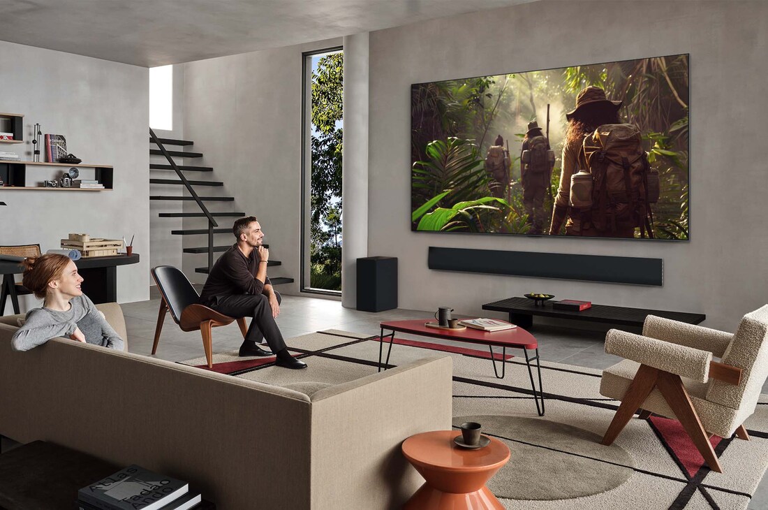 Tampilan ruang tamu yang luas di dalam rumah mewah, seorang pria sedang menonton film di LG OLED TV wall mounted. Desain TV berpadu secara elegan dengan dinding dan desain interior.