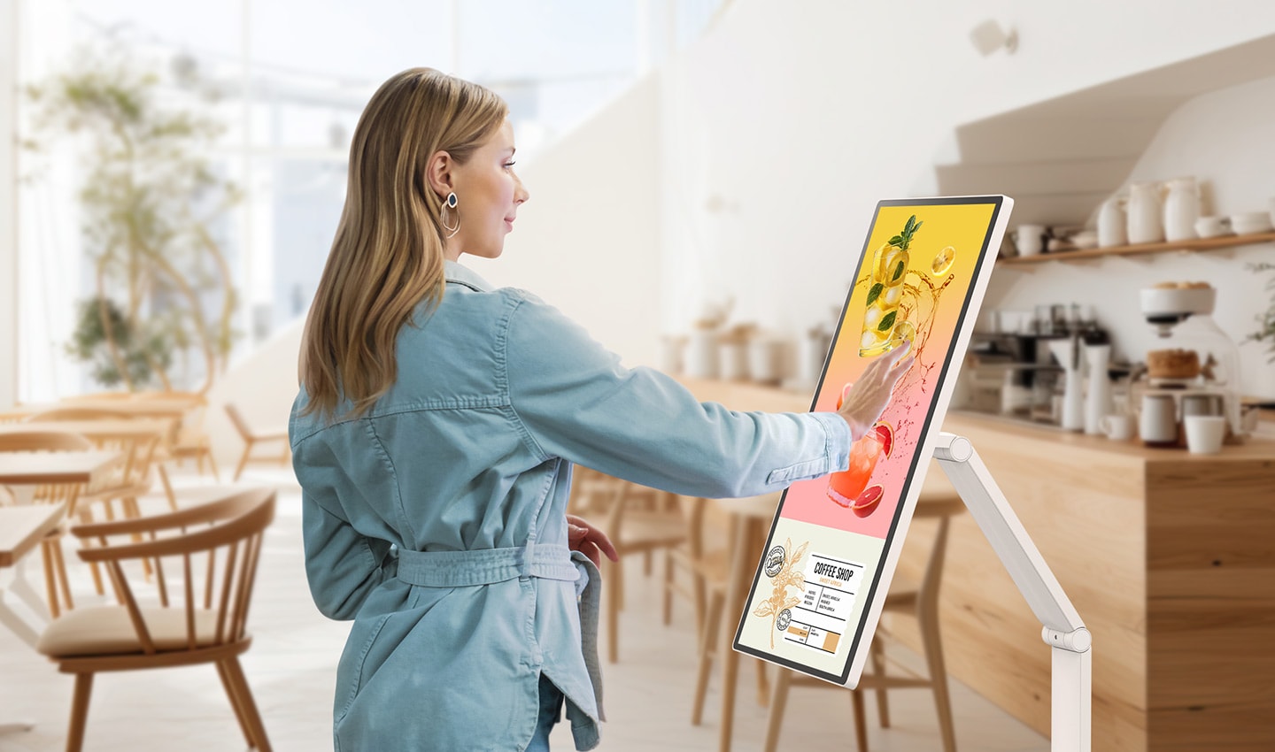 Seorang wanita sedang melihat spanduk acara yang ditampilkan pada LG Smart Monitor Swing di sebuah kafe.