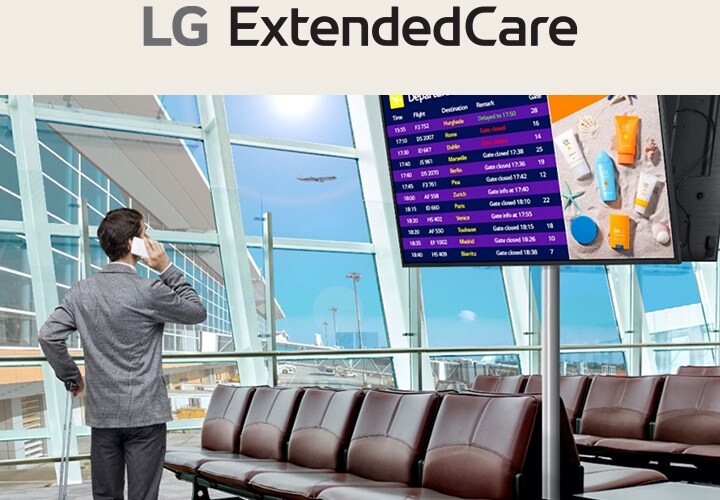 A traveler stands in an airport lounge, checking his phone while looking at a digital departure board displaying flight schedules. The scene highlights the modern, efficient use of signage for real-time updates.