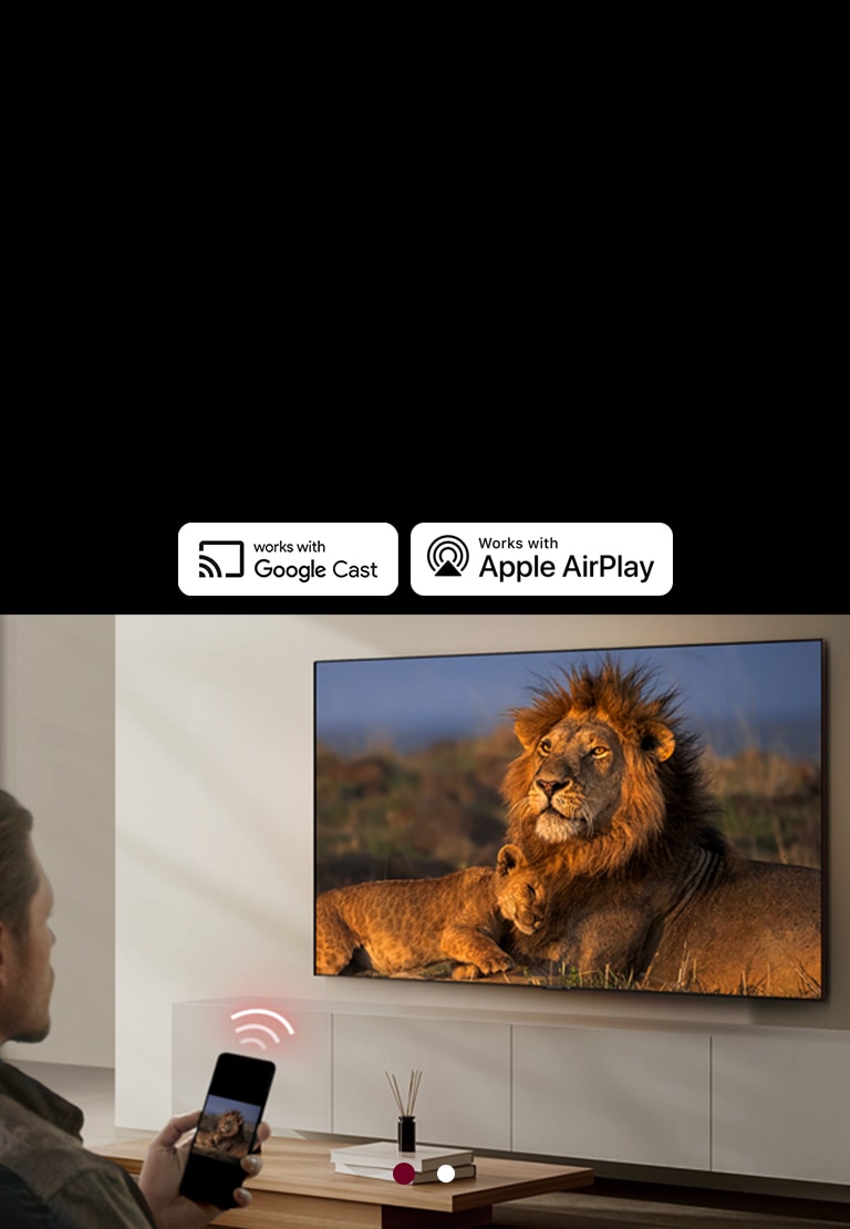 An LG TV mounted on a wall in a living room, displaying a lion and lion cub. A man sits in the foreground with a smartphone in his hand displaying the same image of lions. A graphic of three neon red curved bars is displayed just above the smartphone pointing toward the TV.