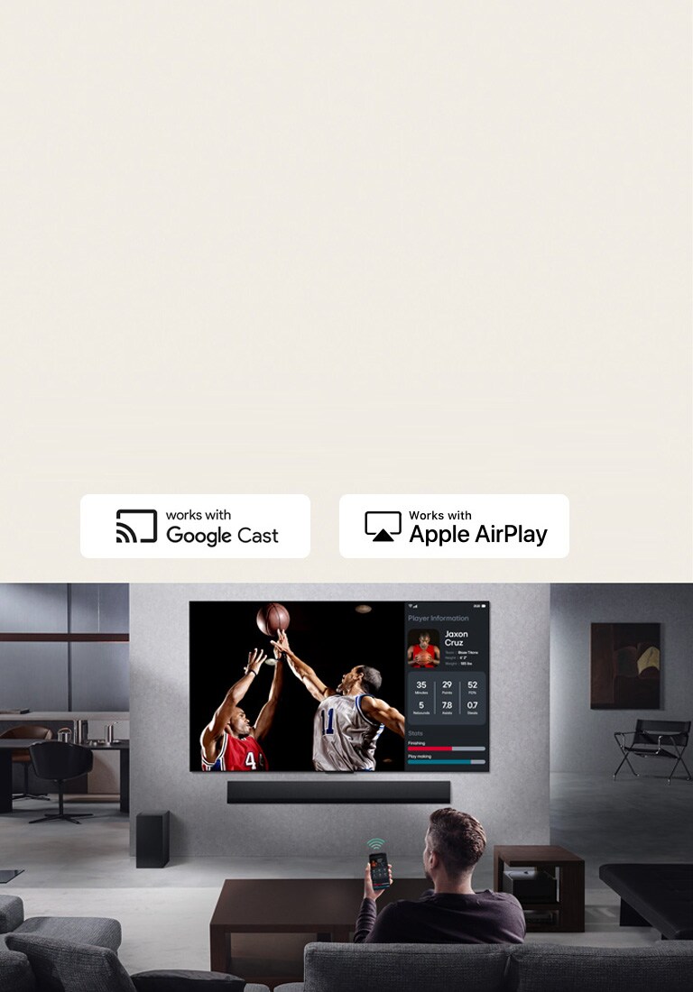 Person in their living room holding their phone. On the phone is a transmitting icon showing that the phone screen is being mirrored on the TV. On the TV is a basketball game to the side is the mirrored screen, showing player statistics. 