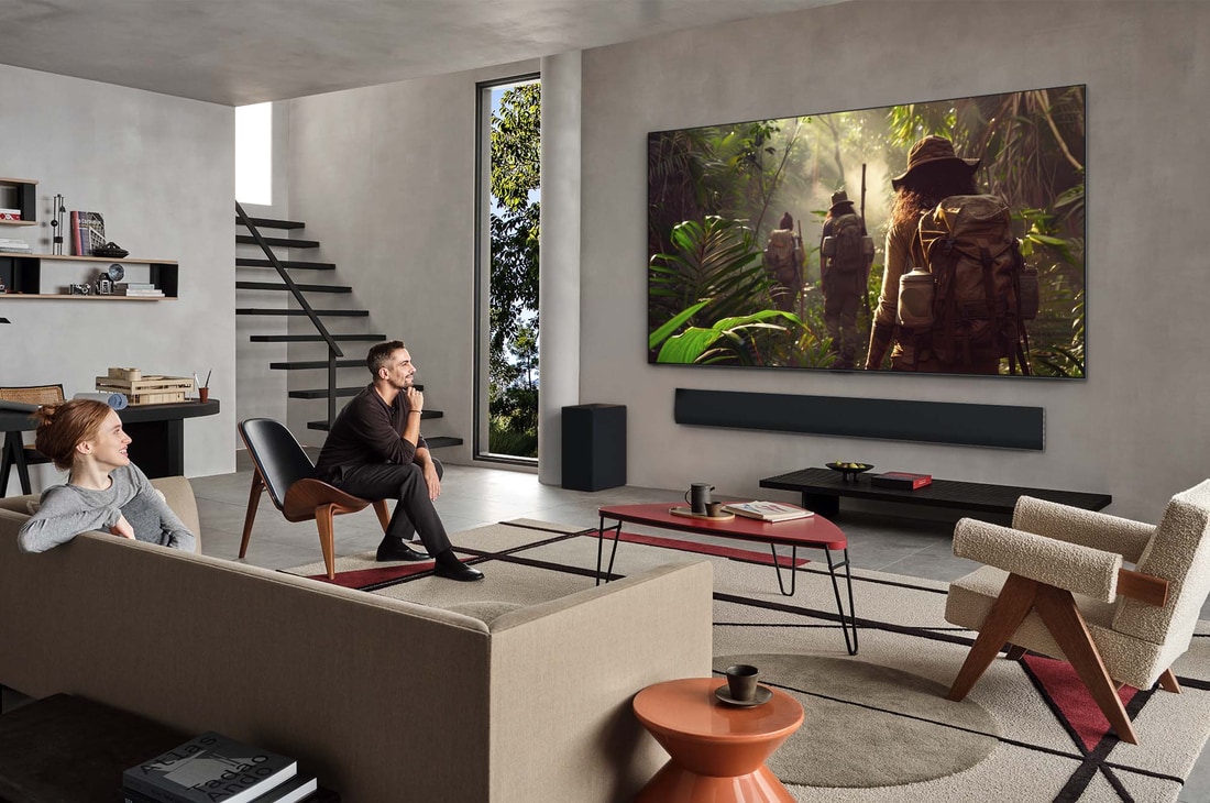 Wide view of a living room inside a premium home, a man is watching a movie on his wall-mounted LG OLED TV. The TV's design blends elegantly with the wall and the interior design.