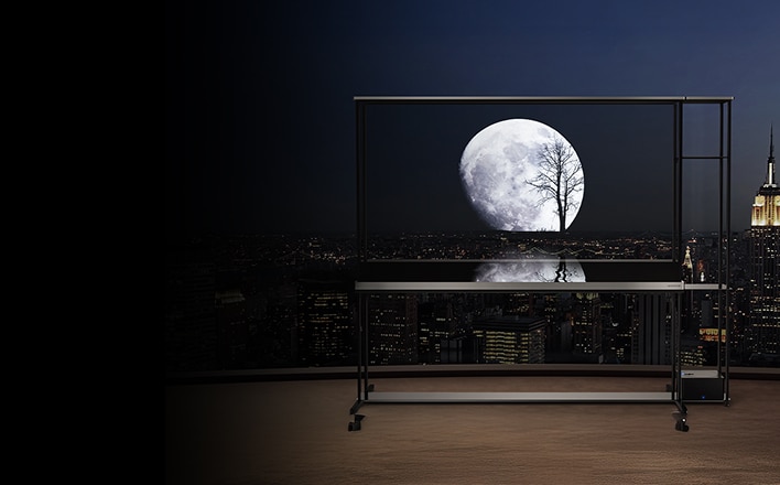 TV trasparente su un balcone di notte che mostra la luna piena e la sagoma di un albero sullo sfondo dello skyline cittadino.