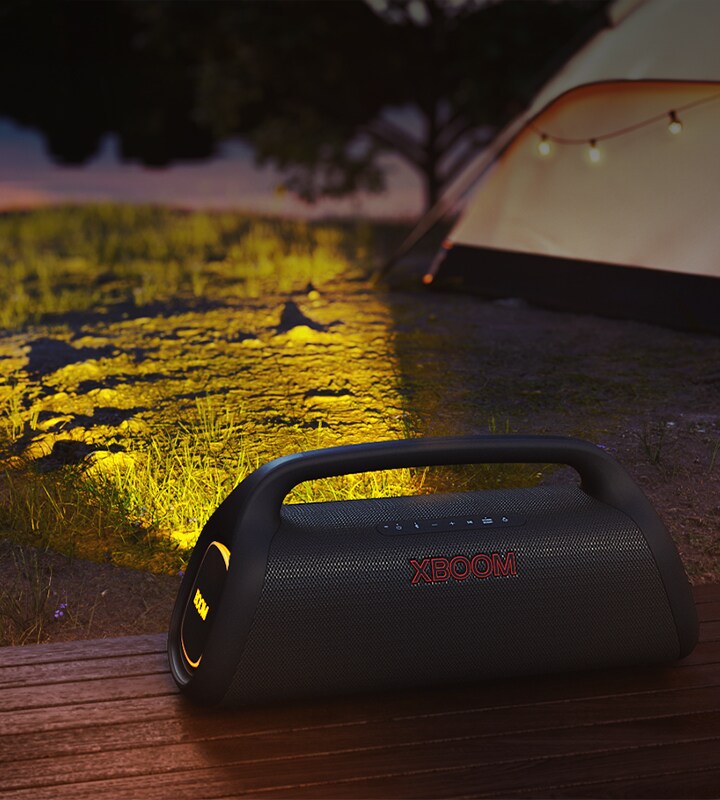Il dispositivo LG XBOOM Go è posizionato su un ripiano in legno. Produce un'illuminazione da spettacolo nella zona del campeggio.