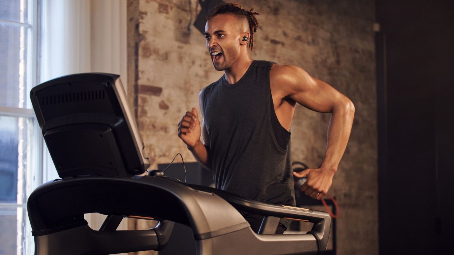 Cosa portare in palestra: immagine di un ragazzo che corre sul tapis roulant e usa le cuffie bluetooth LG.    