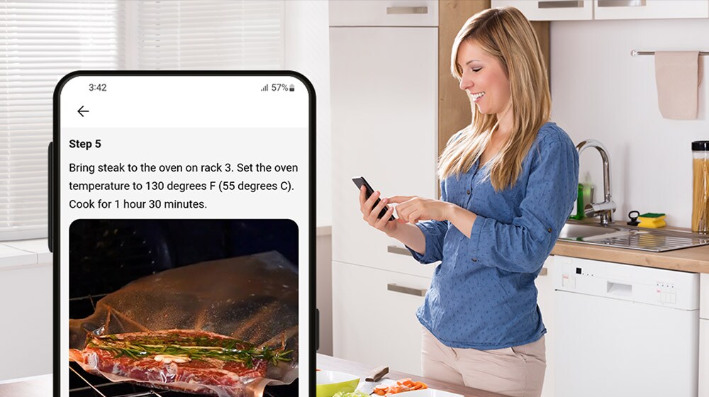  Una donna in una cucina moderna segue una ricetta sullo smartphone per cuocere una bistecca nel forno.