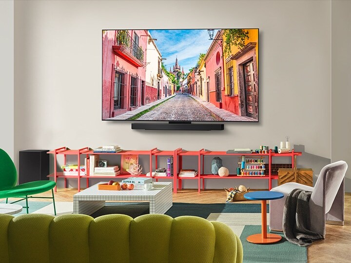 Vista frontale del TV LG OLED con una soundbar montato a parete in un salotto colorato, che mostra il suo design ultra sottile. 