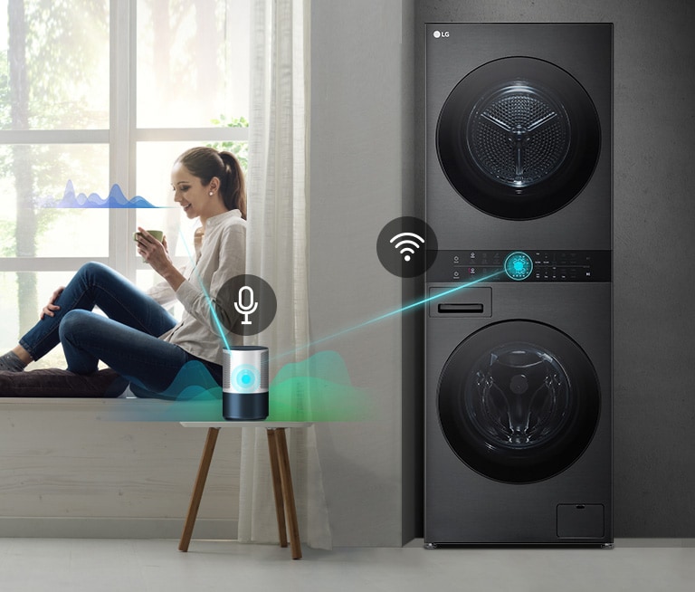 Donna seduta vicino a una finestra usa uno smartphone accanto a una lavatrice e asciugatrice LG nera connessa a Wi-Fi.