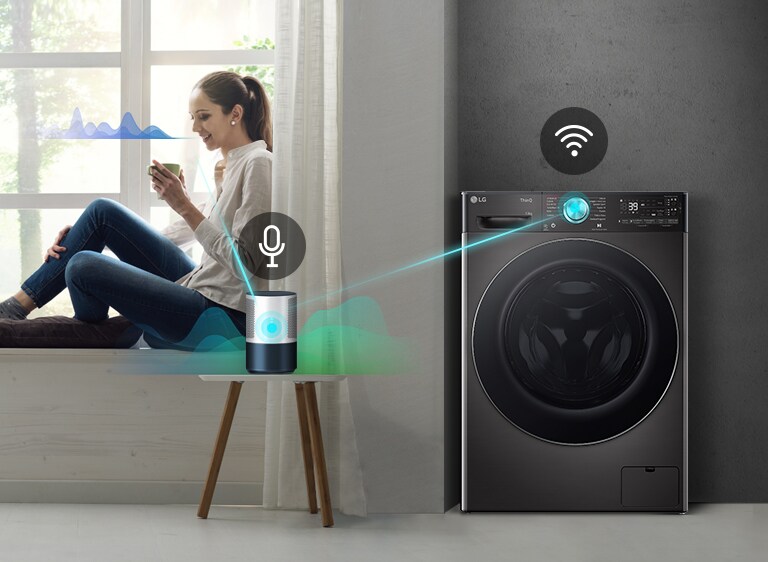 Donna seduta su un davanzale, vicino a una finestra, controlla una lavatrice LG smart tramite uno smart speaker su un tavolo.