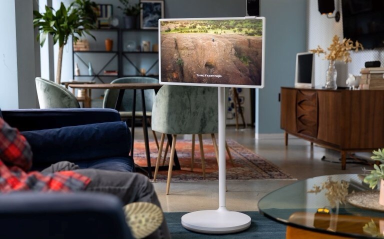 Un soggiorno moderno con una LG StanbyME, un display su supporto mobile che ottimizza lo spazio, mostrando una scena naturale. L'arredamento elegante e compatto crea un ambiente accogliente e funzionale.