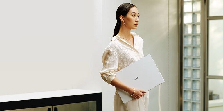 Una donna elegante con in mano un laptop LG Gram, in un ambiente moderno e luminoso.