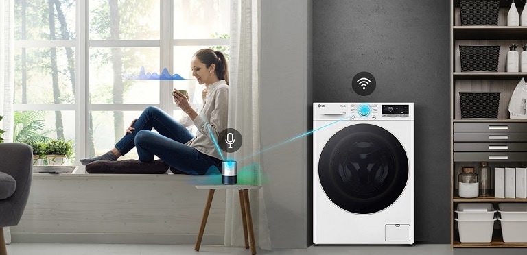 Una donna seduta vicino a una finestra luminosa utilizza un assistente virtuale per controllare una lavatrice LG ThinQ con comandi vocali, mostrando la tecnologia smart home.