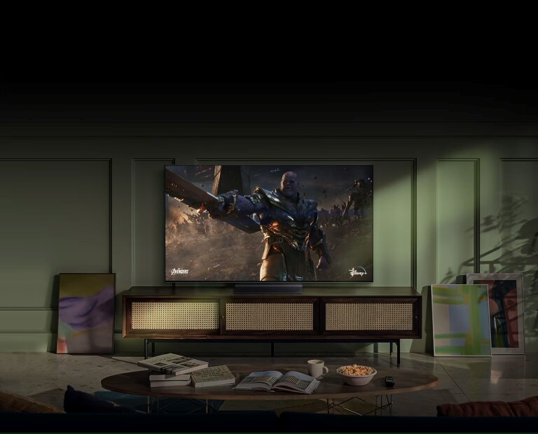 Un soggiorno elegante con una TV LG che mostra una scena epica di un film con un personaggio in armatura. Davanti alla TV, un tavolino con libri, una tazza e dei popcorn, creando un'atmosfera moderna e accogliente.