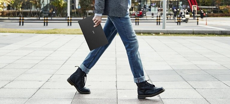 Persona che cammina all'aperto tenendo in mano un laptop.