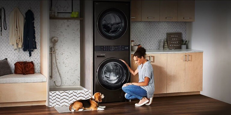  Donna in ginocchio davanti a una washtower LG in una lavanderia moderna, con un cane sdraiato.