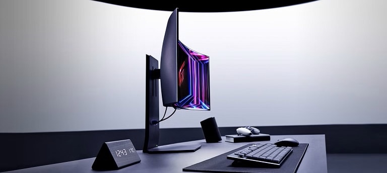 Una configurazione desktop moderna presenta un monitor da gaming curvo LG con colori vivaci, una tastiera, un mouse e un orologio angolato che mostra l'ora. La configurazione è minimalista e professionale.