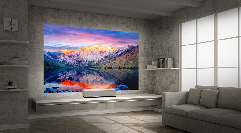 Un impianto di home theater dotato di un grande proiettore che mostra un paesaggio montano vivace su una parete grigia, accanto a un elegante divano grigio e arredi minimalisti.